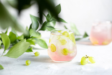 Summer cold lemonade with grapes on a light table among greenery.