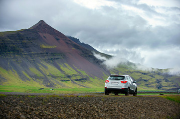 Obraz na płótnie Canvas White cars parked on a dirt road The background is high mountains with green grass all over the area. In the summer and cloudy days in the countryside in Iceland. Concept for traveling on holidays