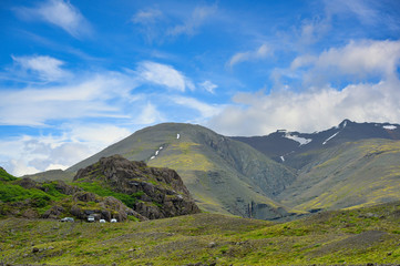 Fototapeta na wymiar Many cars parked on the slopes. The background is high mountains with green grass all over the area. In the summer and blue sky days at countryside in Iceland Concept for traveling on holidays