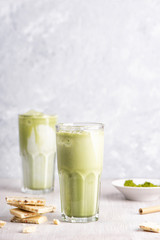 Glasses of matcha latte with coconut milk and white chocolate on wooden and marble background