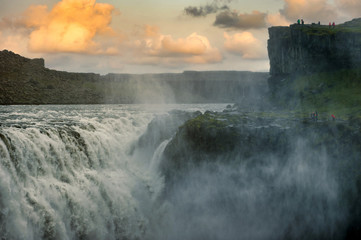 Dettifoss Waterfall in northern Iceland during the summer, evening. There are tourists taking pictures and watching the grandeur. This is an important and popular tourist destination.
