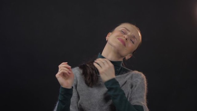 pretty woman with long dark hair in grey sweater holds hands on aching head stretches body and spreads arms close view. Woman emotion
