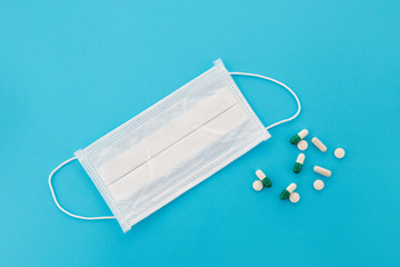 Top view of a medical surgical mask and one of many colorful pills on the side. A disposable doctor's respirator