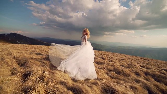 attractive young bride with white hair in a wedding dress walks or runs on the mountain, ha background of mountains and rocks landscape, dramatic sky. slow motion
