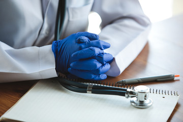Close up of doctors hands wearing blue protective gloves on wooden table background. Preparing for...