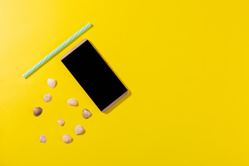 Beach accessories on a yellow background - snails, plastic straw, smartphone. Summer is coming...