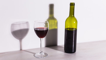 A glass of wine and a bottle casts a long shadow from the evening sun.