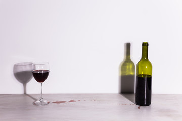 Bottle with wine and glass, red puddle of wine on the table. Cleaning after party concept.
