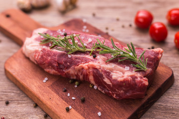 Raw meat. A large piece of beef chop on a wooden cutting board with rosemary and spices, close-up.
