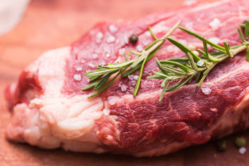 Raw meat. A large piece of beef chop on a wooden cutting board with rosemary and spices, close-up.