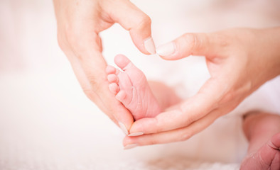 Legs newborn baby hands hug mother, forming a heart. Symbolizes love, unity, caring, tender to the baby. New family concept.