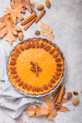 Pumpkin Pie and slice  with pecan nut and cinnamon on gray concrete background, top view, copy space. Homemade autumn pastry for Thanksgiving