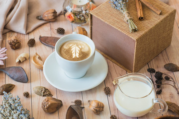 A cup of coffee, milk, gift box, and decoration on a wooden background. Autumn composition top view. Details of still life with decoration. Cozy breakfast