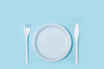 Plato redondo de plástico desechable con tenedor y cuchillo sobre fondo celeste aislado. Vista...