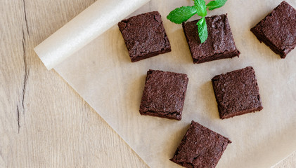 Freshly baked classic fudge brownie on parchment brown paper and wooden table background. Homemade sweet food. 