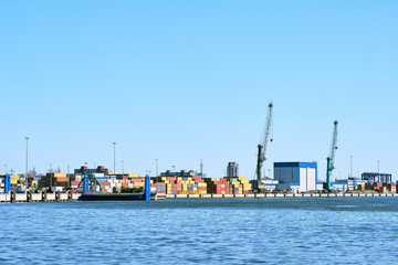 Fototapeta premium View of port cranes, loading bridges and container terminal on clear sunny day and cloudless sky. Sea trade, transportation, commerce and cargo