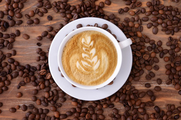 Cup of tasty cappuccino and coffee beans on wooden background