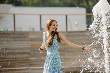 Girl in a blue dress having fun among the fountains