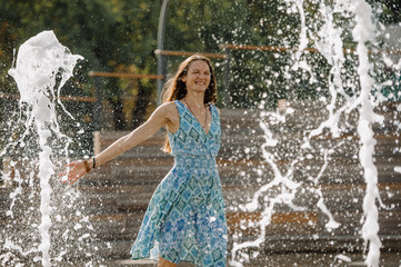 Girl in a blue dress having fun among the fountains