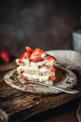 cake with fresh strawberries and cream cheese on wooden board, rustic wooden background, seasonal dessert
