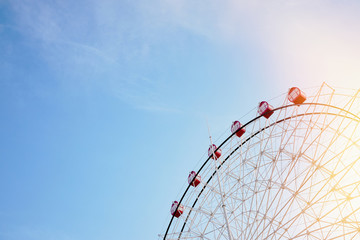 Ferris wheel with bright red booths on background of serene clear blue sky with sunflare as symbol of joy recreation relaxation fun and good time with copy space.