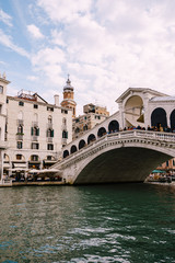 Fototapeta na wymiar The beautiful Ponte di Rialto Bridge over the Central Grand Canal in Venice, Italy, with shops, beautiful views and lots of people. Near boat station of the same name, the street leads to San Marco