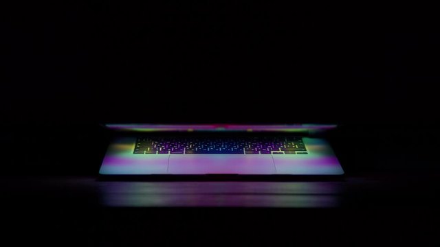 Almost closed laptop screen lit up keyboard reflection of colorful shapes and forms. Concept future technology and commercial. Night screensaver video of millennial generation tool
