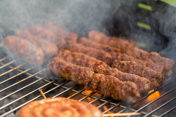 Sausages and traditional romanian sausages called ”mici” or ”mititei” (dish consisting of grilled ground meat rolls in cylindrical shape made from a mixture of meat and spices) on barbecue with smoke