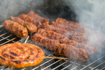 Sausages and traditional romanian sausages called ”mici” or ”mititei” (dish consisting of grilled ground meat rolls in cylindrical shape made from a mixture of meat and spices) on barbecue with smoke