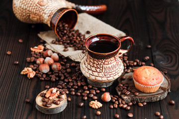 Obraz na płótnie Canvas hot fragrant coffee in a vintage clay cup and coffee beans with nuts on a dark wooden background