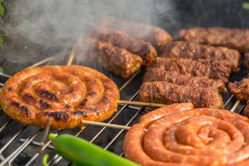 Sausages and traditional romanian sausages called ”mici” or ”mititei” (dish consisting of grilled ground meat rolls in cylindrical shape made from a mixture of meat and spices) on barbecue with smoke