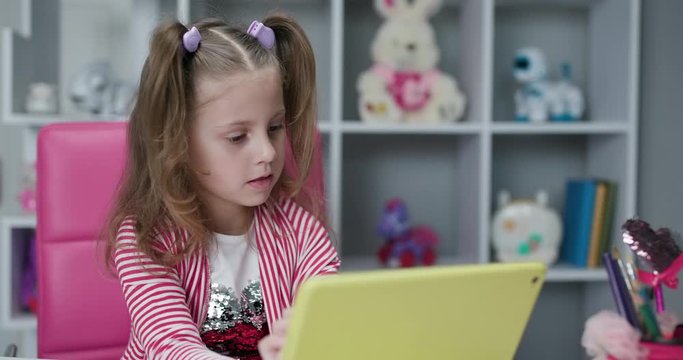 Small child hold pad computer surfing internet play game at home. Children tech addiction concept. Curious cute preschool kid girl using digital tablet technology device.