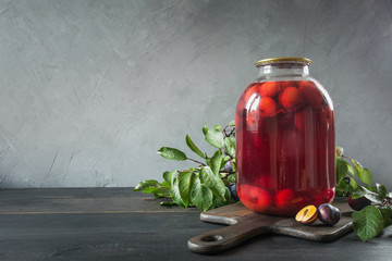 Homemade canned plum compote in large glass jar on wooden board. Space for text. Rustic style.