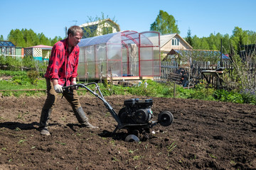 Old man plows the ground with a motor cultivator. A farmer ploughs the soil using a petrol...