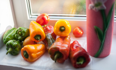 Green, yellow and red bell peppers, illuminated by sunlight, on the kitchen windowsill.