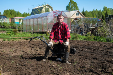 Old man plows the ground with a motor cultivator. A farmer ploughs the soil using a petrol...