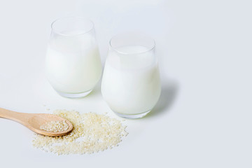 Two glass of vegatarian rice milk and rice grains on white background. Non dairy alternative milk. Concept of proper nutrition and healthy eating. Organic food. Copy space for text, selective focus