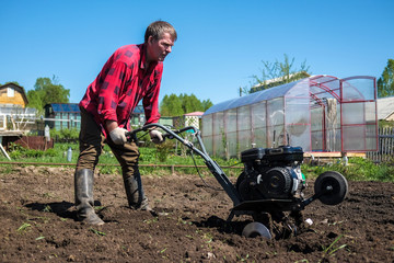 Old man plows the ground with a motor cultivator. A farmer ploughs the soil using a petrol cultivator.