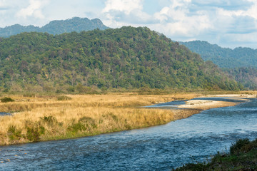 scenic landscape of Ramganga River, mountains and clouds in sky at dhikala zone of corbett national park or tiger reserve, uttarakhand, india