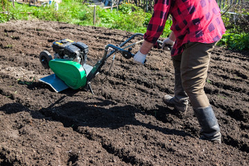 Old man plows the ground with a motor cultivator. A farmer ploughs the soil using a petrol...