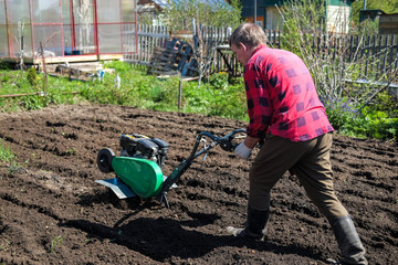 Old man plows the ground with a motor cultivator. A farmer ploughs the soil using a petrol...