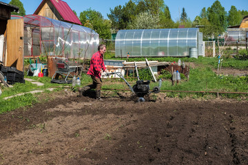 Old man plows the ground with a motor cultivator. A farmer ploughs the soil using a petrol...