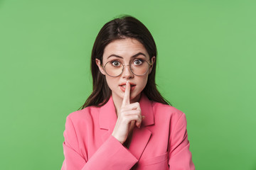 Image of excited young woman in eyeglasses making silence gesture