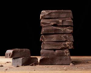 broken black chocolate on a wooden table, culinary sweet ingredient