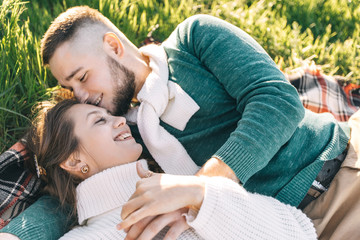 A guy and a girl love each other, smile, hug, kiss, laugh, enjoy life in the forest on a cliff, in the grass. Girl holding a film camera in her hands, photographs a guy, sunset in the background.
