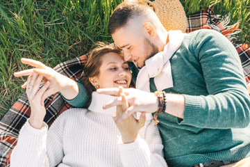 A guy and a girl love each other, smile, hug, kiss, laugh, enjoy life in the forest on a cliff, in the grass. Girl holding a film camera in her hands, photographs a guy, sunset in the background.
