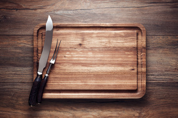 Empty vintage wooden cutting board with roast knife and fork on wooden table