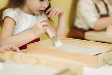 Kids in class create drawing by sand. Children use tassel for rawing. Preschool