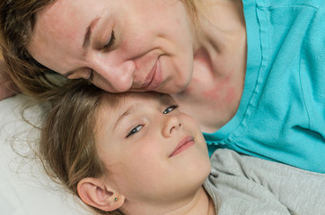 Young mother and daughter lie in bed on a pillow and hugging, happy family