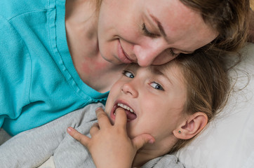 Young mother and daughter lie in bed on a pillow and hugging, happy family